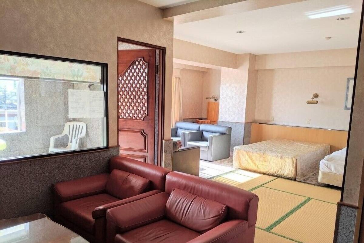 Habitación de hotel con un sofá de cuero rojo, una cama, una mesita y vistas a través de una ventana.