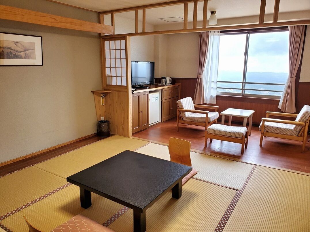 Ein traditioneller japanischer Raum mit Tatami-Böden, einem Fernseher, einem Esstisch und Meerblick.