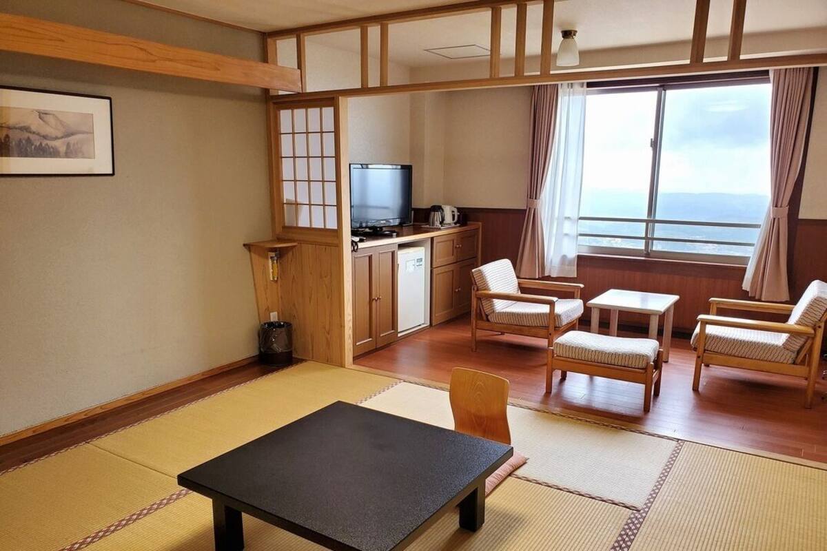 Ein traditioneller japanischer Raum mit Tatami-Böden, einem Fernseher, einem Esstisch und Meerblick.