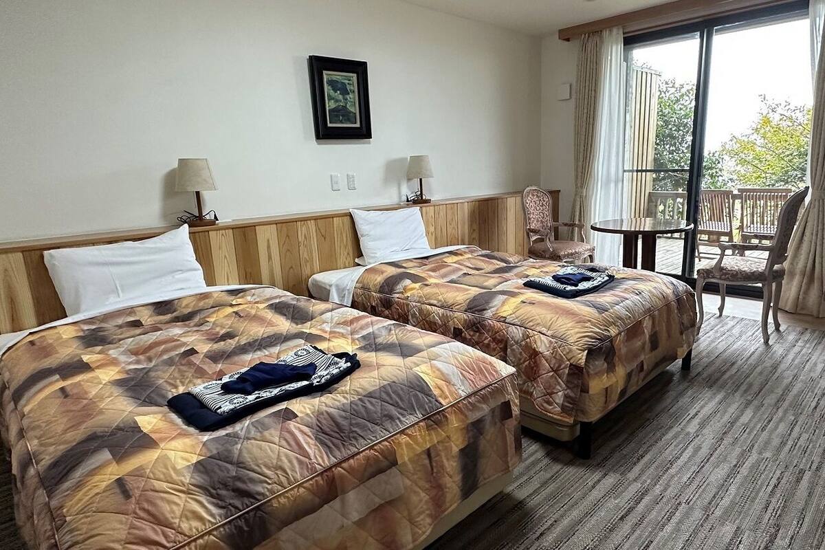 Une chambre d’hôtel avec deux lits, une petite table, une chaise et un balcon avec vue.