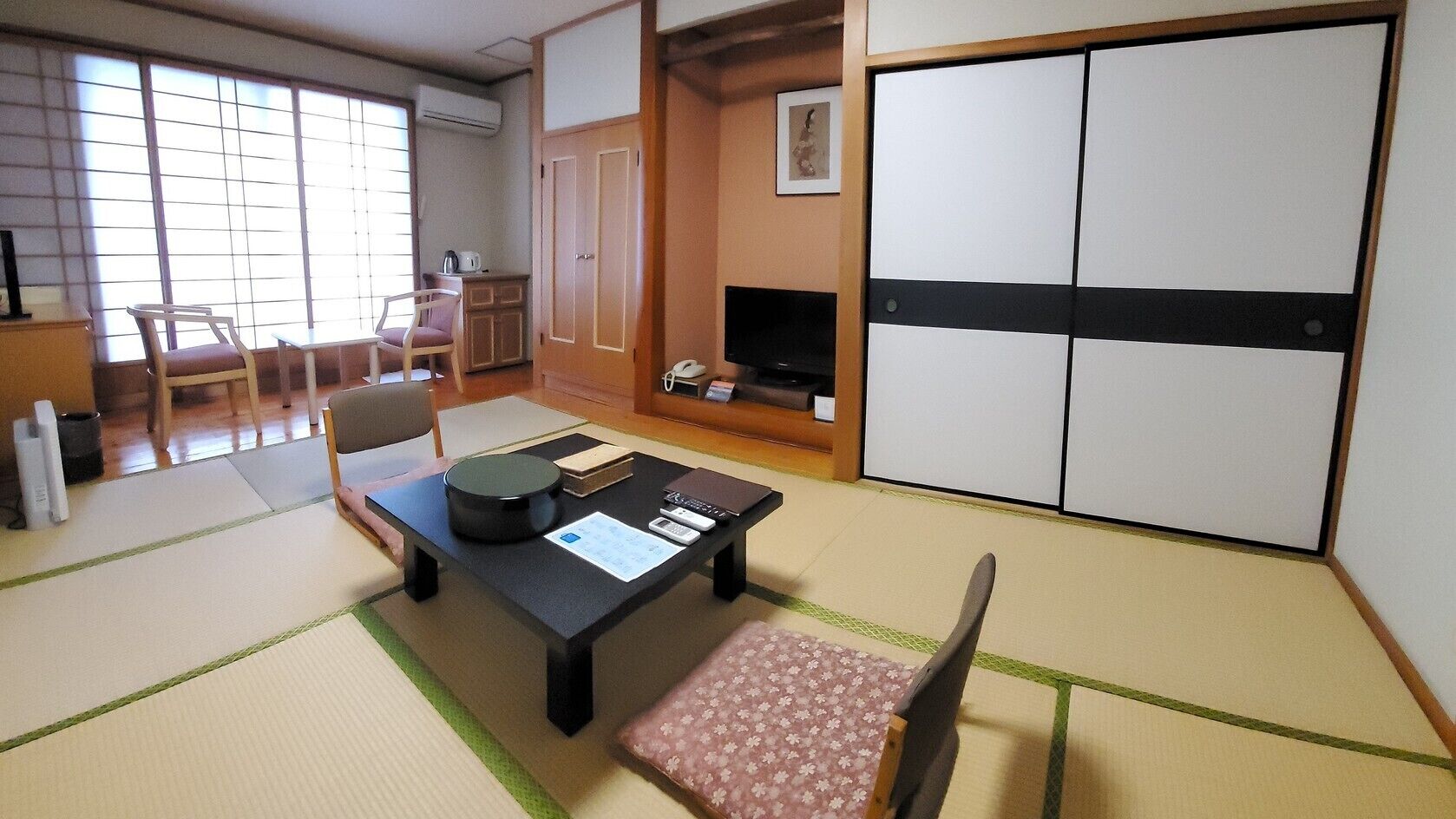 A traditional Japanese room with tatami flooring, a tatami mat table, a television, a wardrobe, and a sliding door.