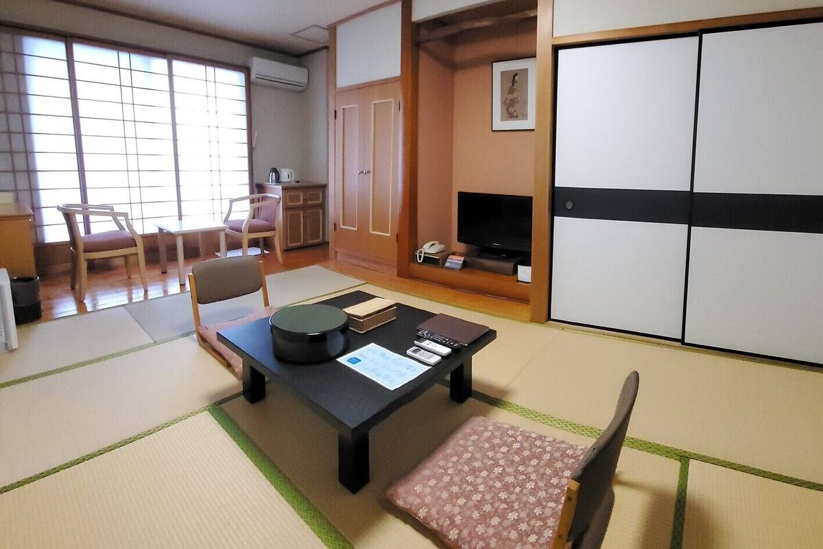 Une pièce de style japonais traditionnel, avec un sol recouvert de tatamis, une table basse en tatami, un téléviseur, une armoire et une porte coulissante.