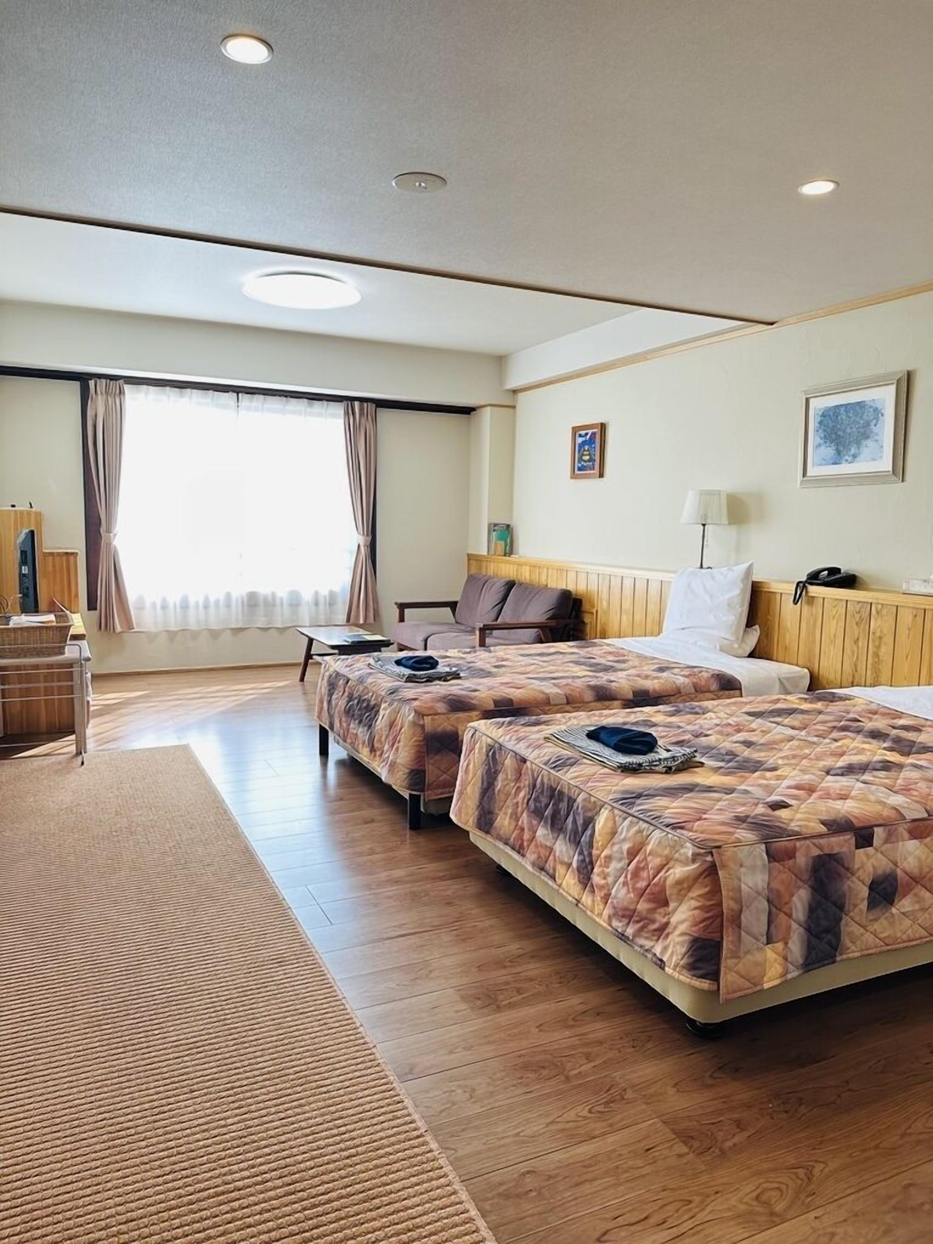 Een hotelkamer met twee bedden, een bureau, een stoel, een raam met gordijnen en een muur met een lijst eromheen.