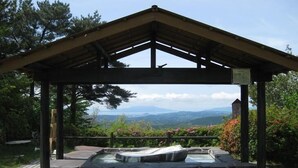 A wooden gazebo with a stone hot tub, surrounded by lush greenery and a mountainous backdrop. - Kirishima Onsen Ryokojin Sanso (Kirishima)