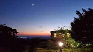 A night scene with a lit building, a visible moon, and distant city lights. - Kirishima Onsen Ryokojin Sanso (Kirishima)