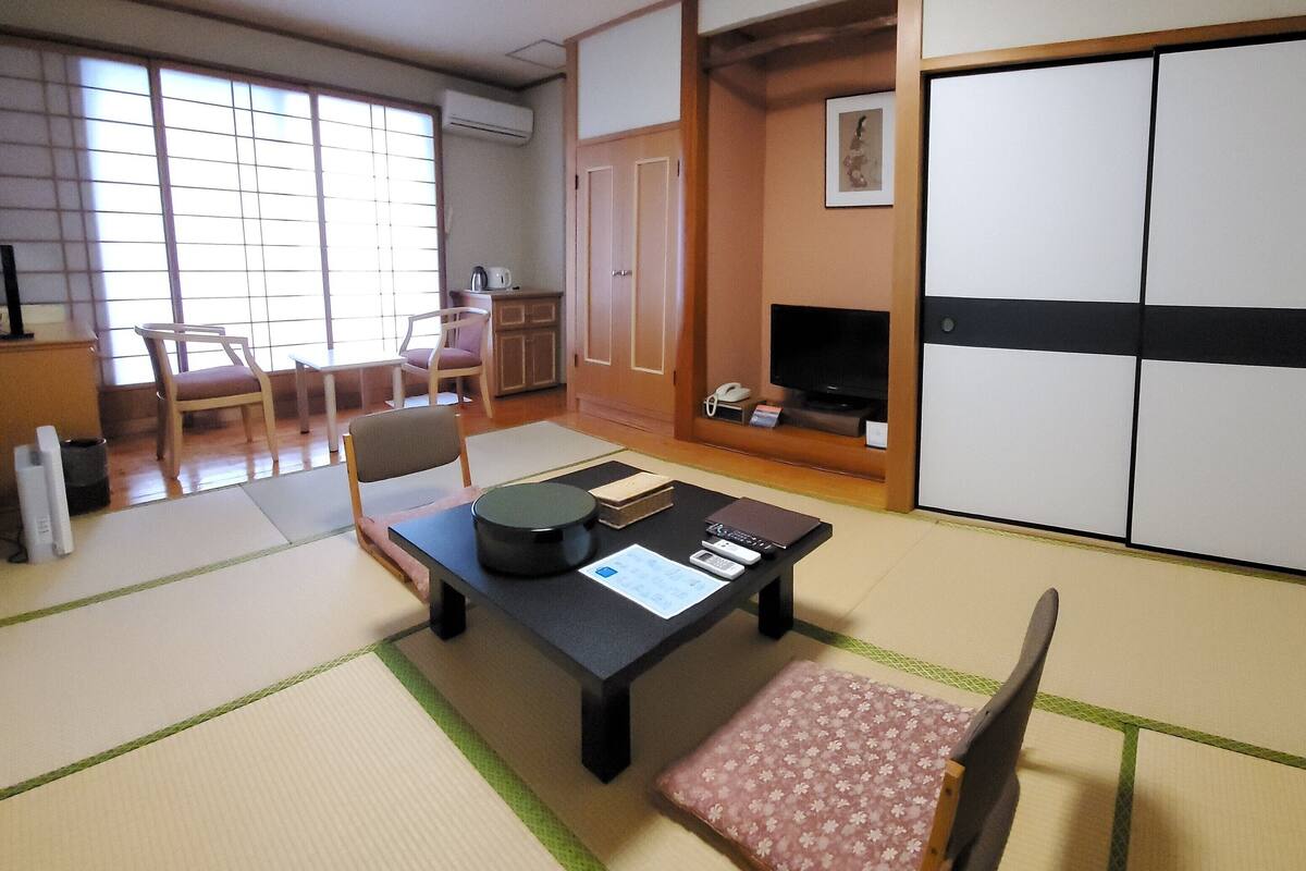 Une pièce de style japonais traditionnel, avec un sol recouvert de tatamis, une table basse en tatami, un téléviseur et un placard à portes coulissantes.