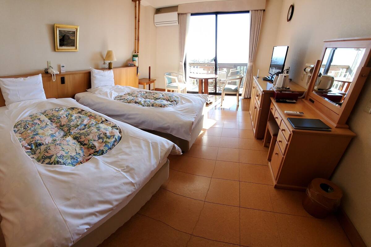 Une chambre d’hôtel avec deux lits, un bureau avec un ordinateur, une télévision et un balcon avec vue.