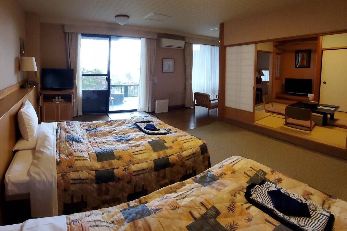 Une chambre d’hôtel avec deux lits, une télévision, un bureau, une chaise et un balcon.