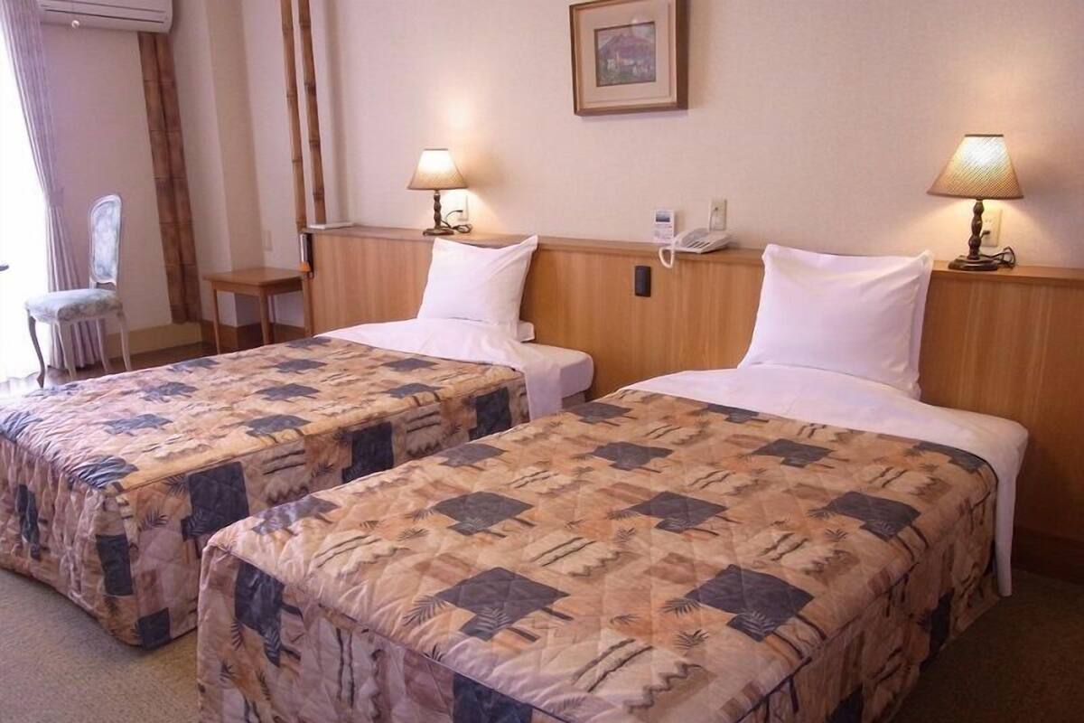 Une chambre d’hôtel avec deux lits, chacun recouvert d’une couvre-lit à motifs, dotée de lampes de chevet, d’un téléphone et d’un tableau encadré au mur.