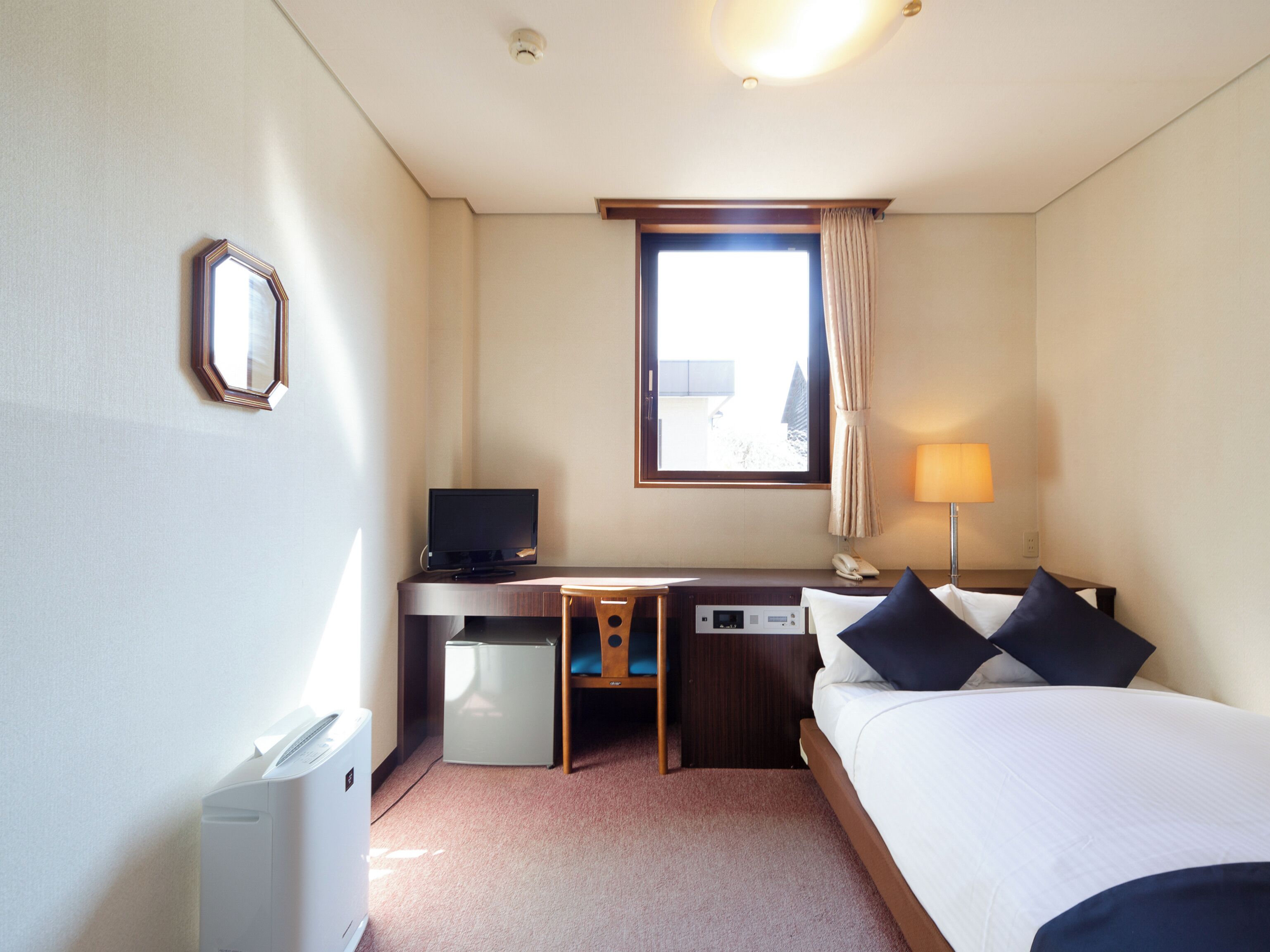 A hotel room with a bed, desk, chair, TV, lamp, and a small refrigerator.