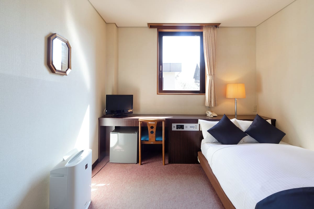 Une chambre d’hôtel équipée d’un lit, d’un bureau, d’une chaise, d’une télévision, d’une lampe et d’un petit réfrigérateur.