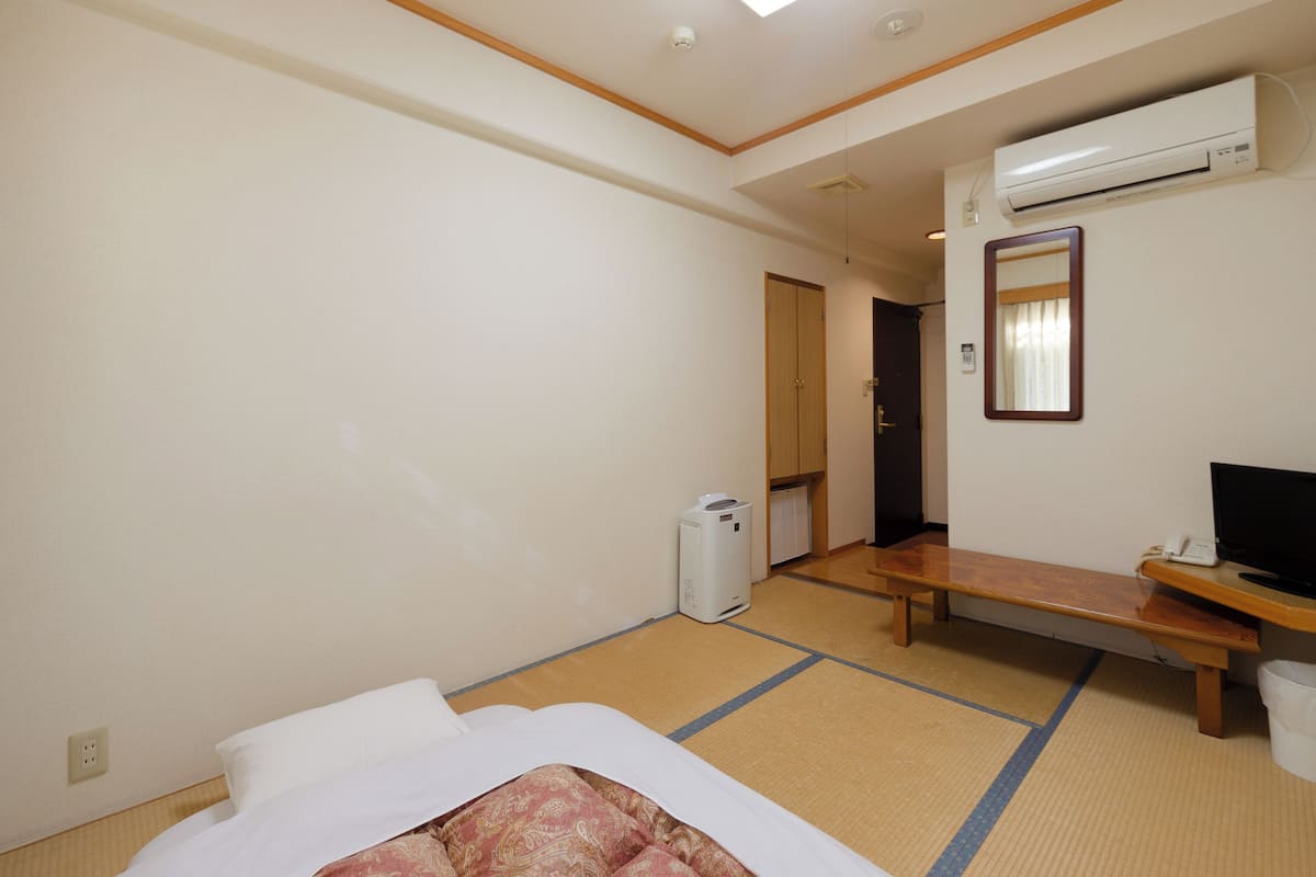 Une chambre d’hôtel équipée d’un lit, d’un bureau, d’un climatiseur, d’un miroir et d’une porte donnant sur une autre chambre.