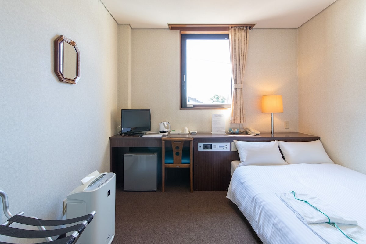 Une chambre d’hôtel équipée d’un lit, d’un bureau, d’une chaise et d’un petit réfrigérateur.