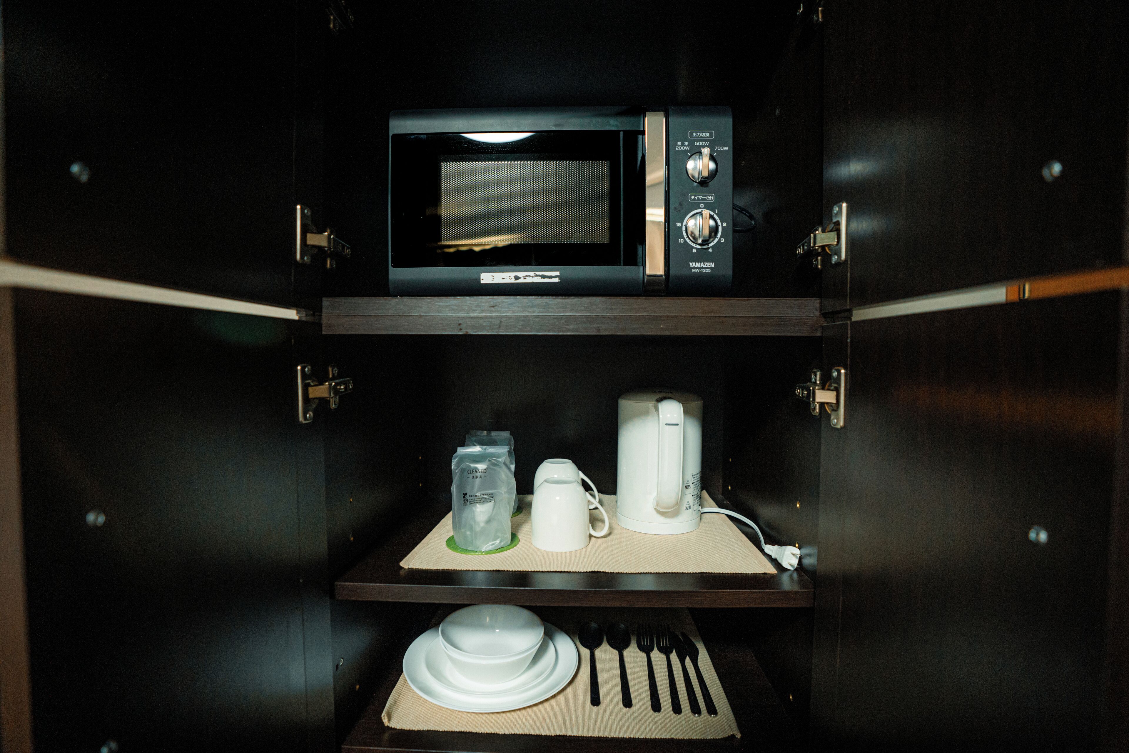A microwave and a coffee maker on a shelf, with a set of dishes and utensils below.