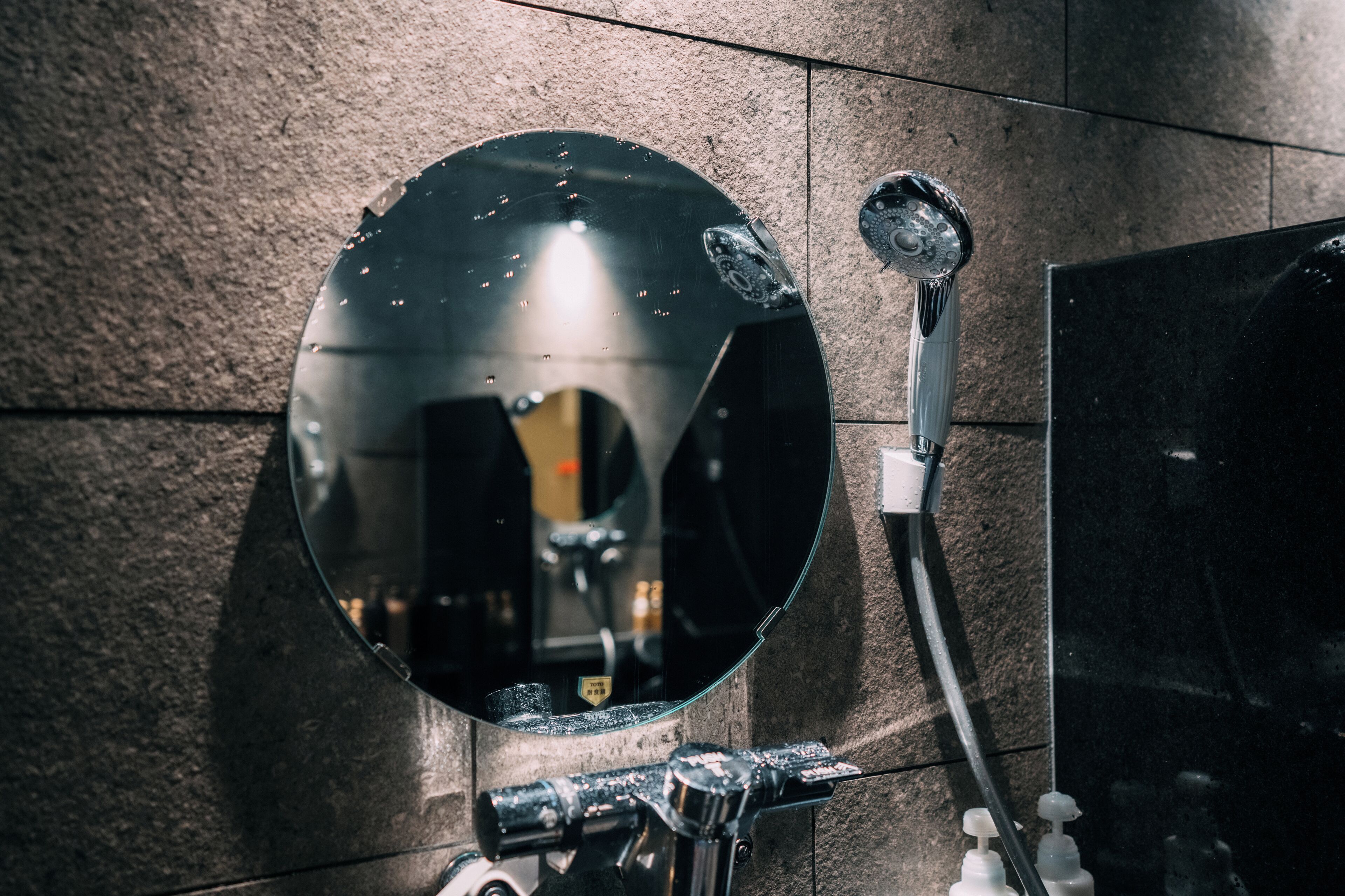 Une salle de bain avec un miroir rond, une douchette à main et un robinet fixé au mur.