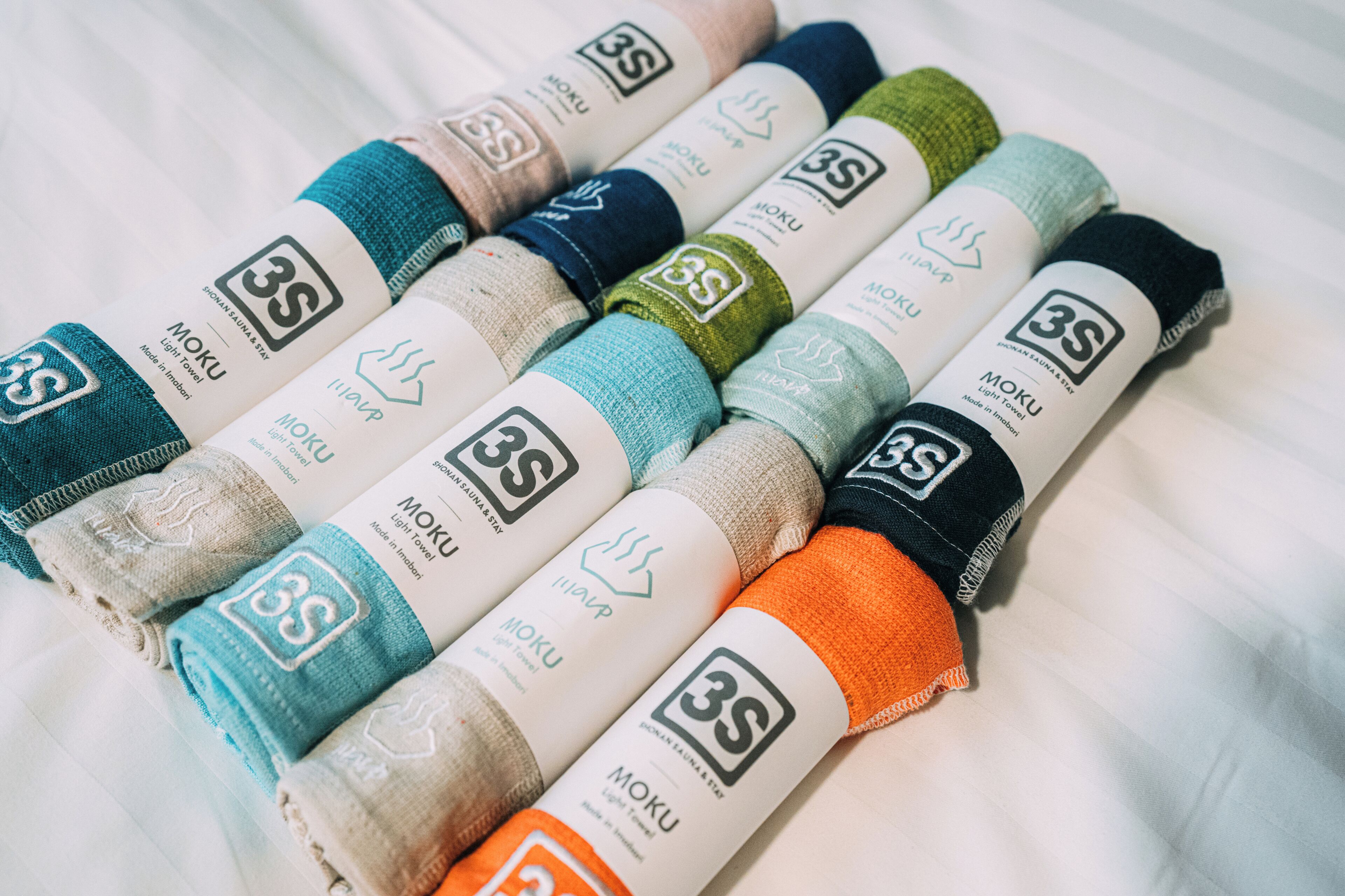 Una colección de calcetines enrollados cuidadosamente, en varios colores y diseños, cada uno con una etiqueta que indica la marca 'MOKU' y la talla '3S'.