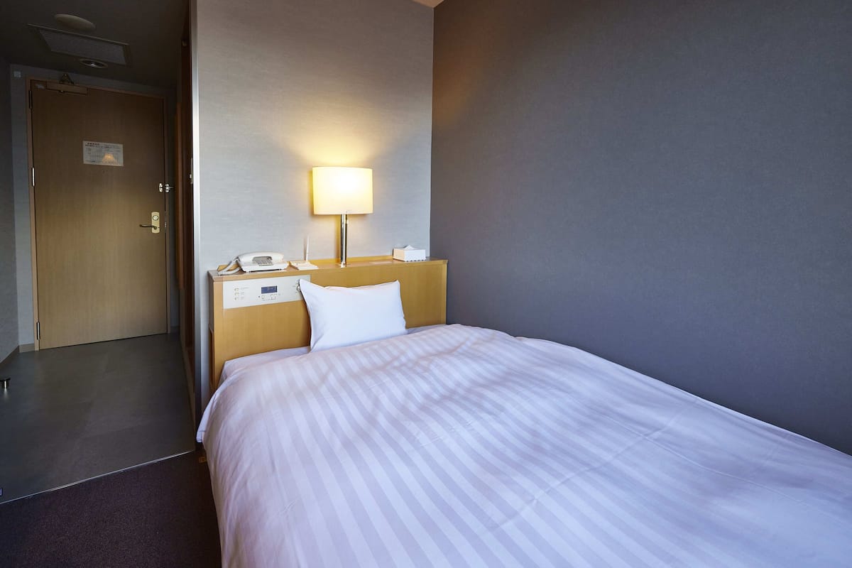A hotel room with a bed, a bedside lamp, a telephone, and a door.