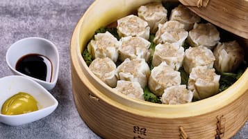 Una vaporera de bambú llena de dumplings, un tazón pequeño de salsa de soja y un tazón pequeño de mostaza.