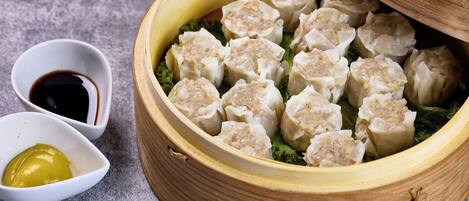 Um cestinho de bambu cheio de dumplings, uma pequena tigela de molho de soja e uma pequena tigela de mostarda.