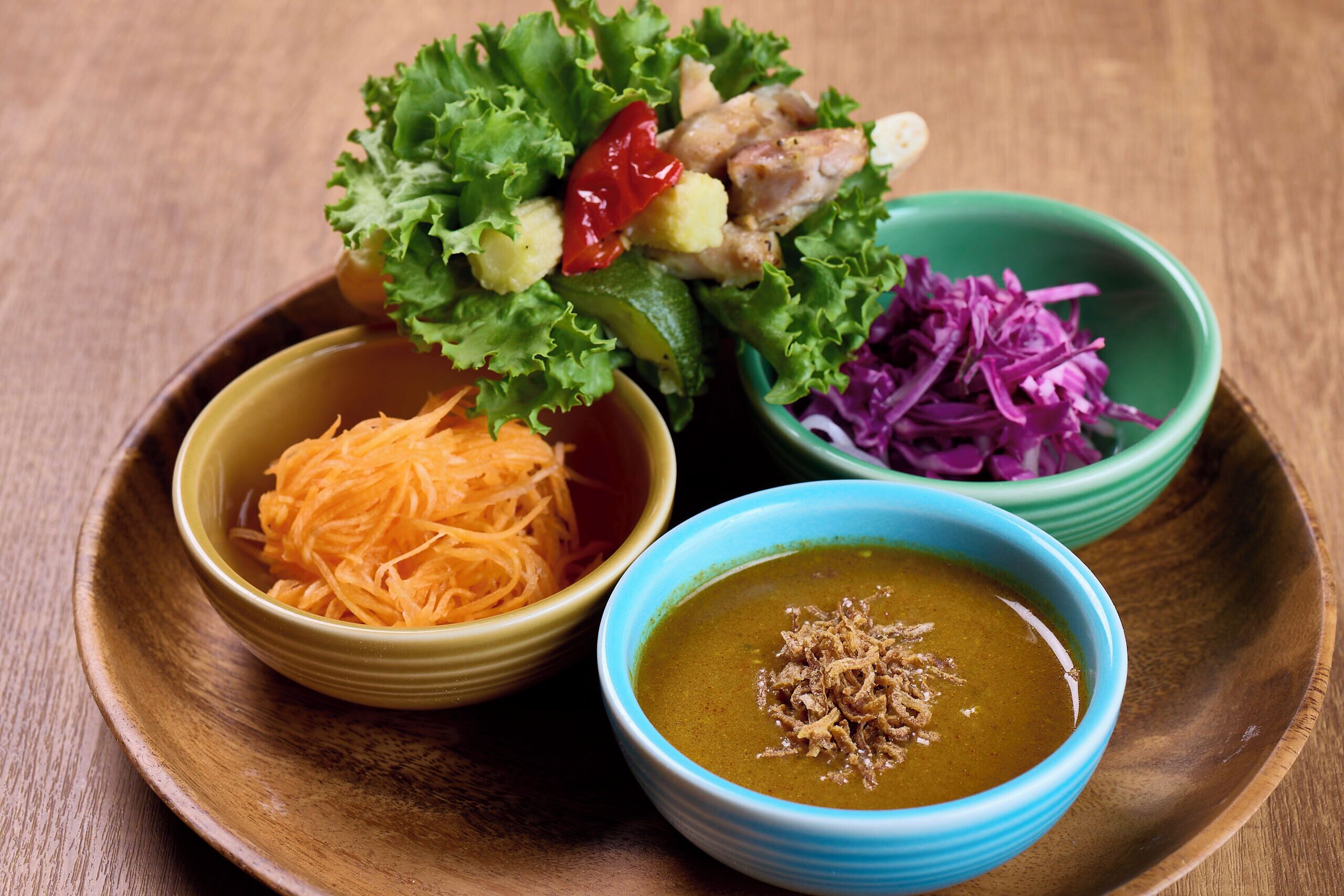 A wooden table with a variety of dishes including shredded carrots, a bowl of soup, and a salad with lettuce and red cabbage.