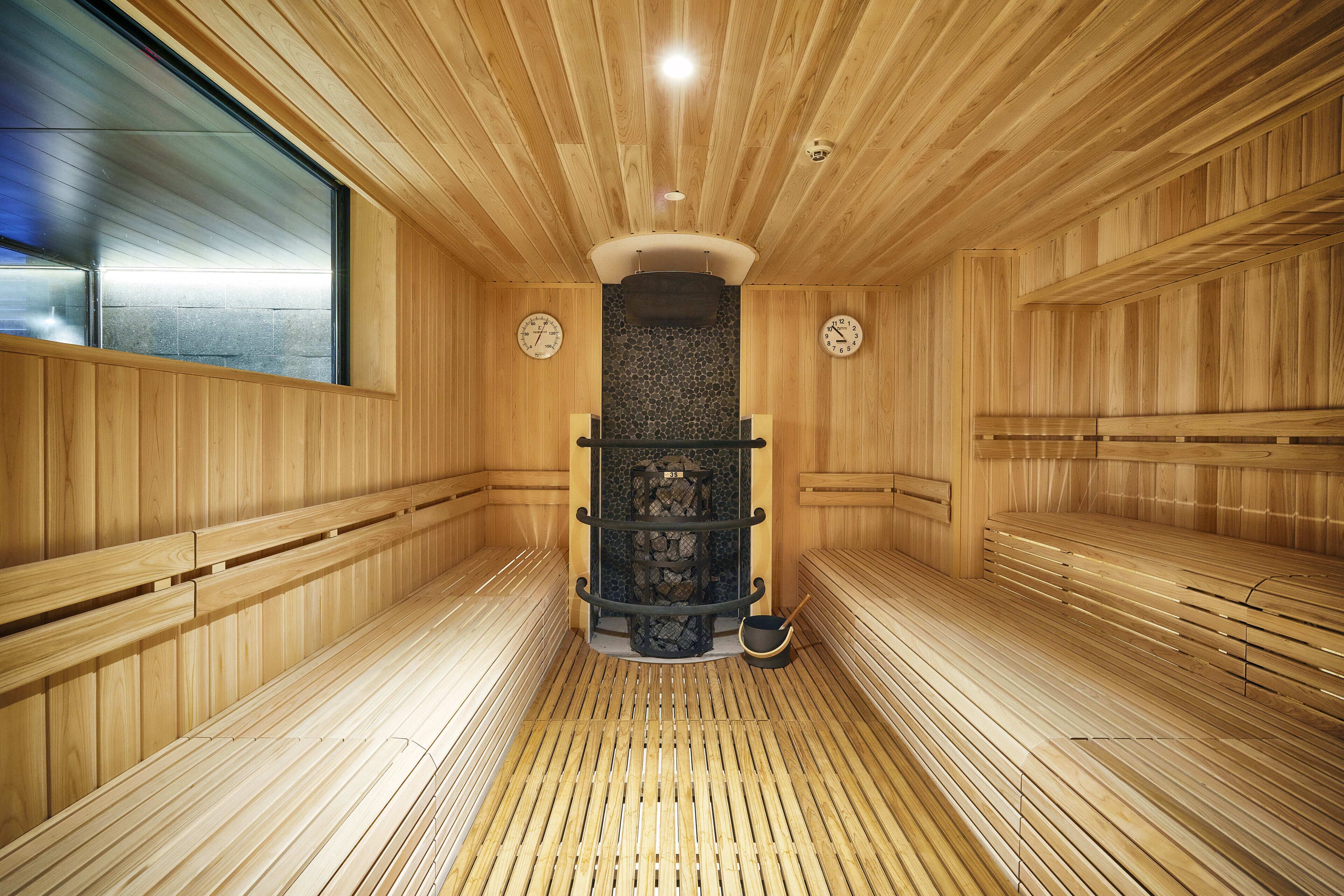 Un sauna avec des murs et des bancs en bois, un mur de pierre au centre et une fenêtre sur le côté gauche.