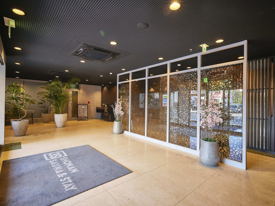 A modern lobby with a reception desk, potted plants, and a glass partition with decorative patterns.