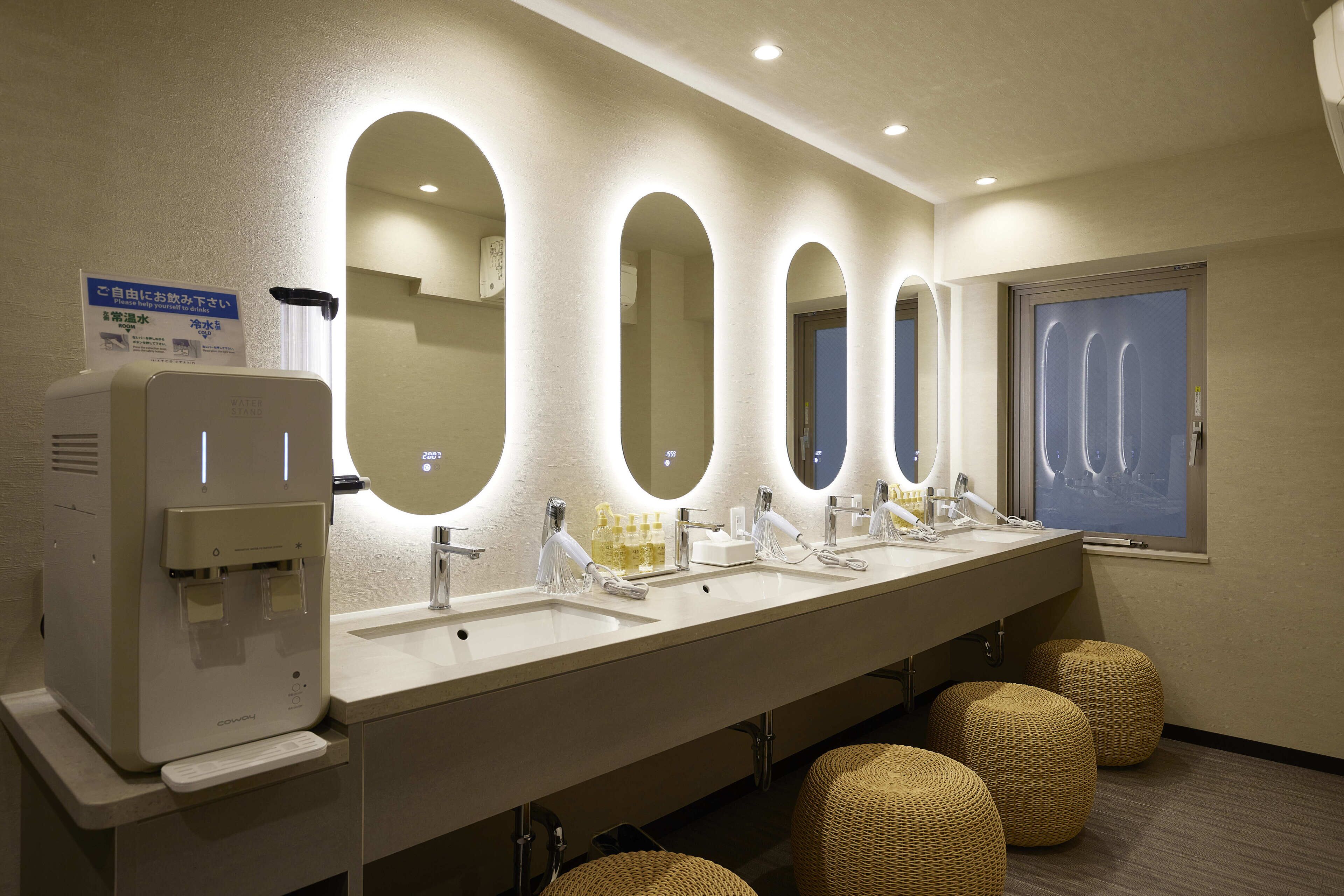 A hotel bathroom with multiple sinks, a hand dryer, and a window.