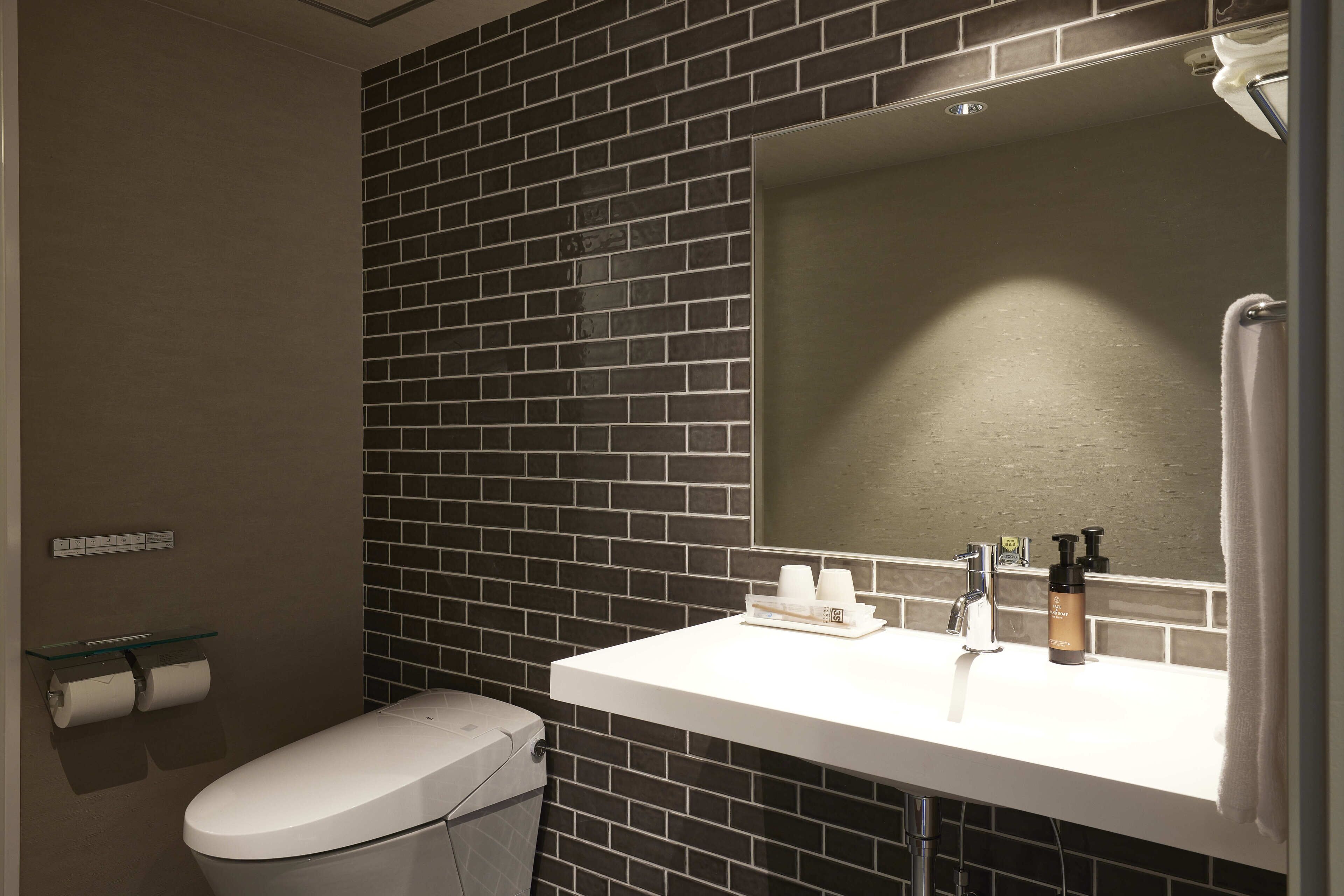 Ein Badezimmer mit einem weißen Waschbecken, dunklen Fliesenwänden, einer Toilette und einem Spiegel.