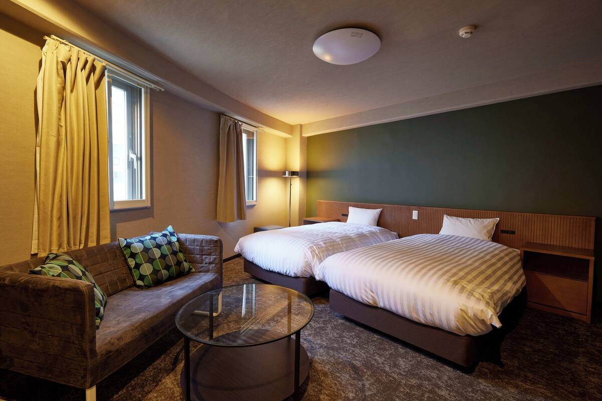 A hotel room with two beds, a sofa, a glass coffee table, and a lamp.