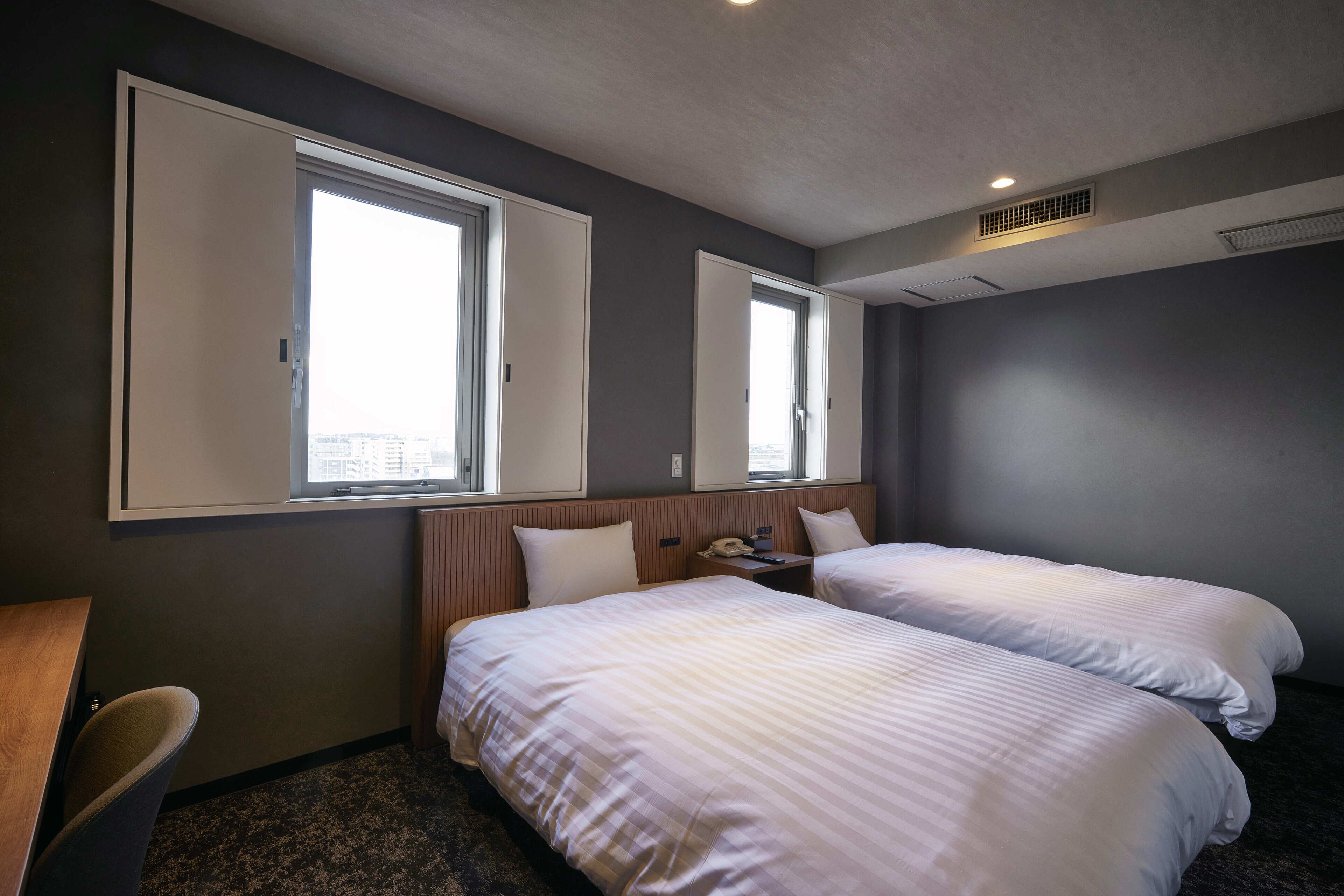 A hotel room with two beds, a desk, and a window.