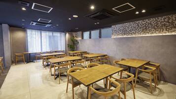 A dining area with multiple wooden tables and chairs, a large window with blinds, and a decorative wall with circular patterns.