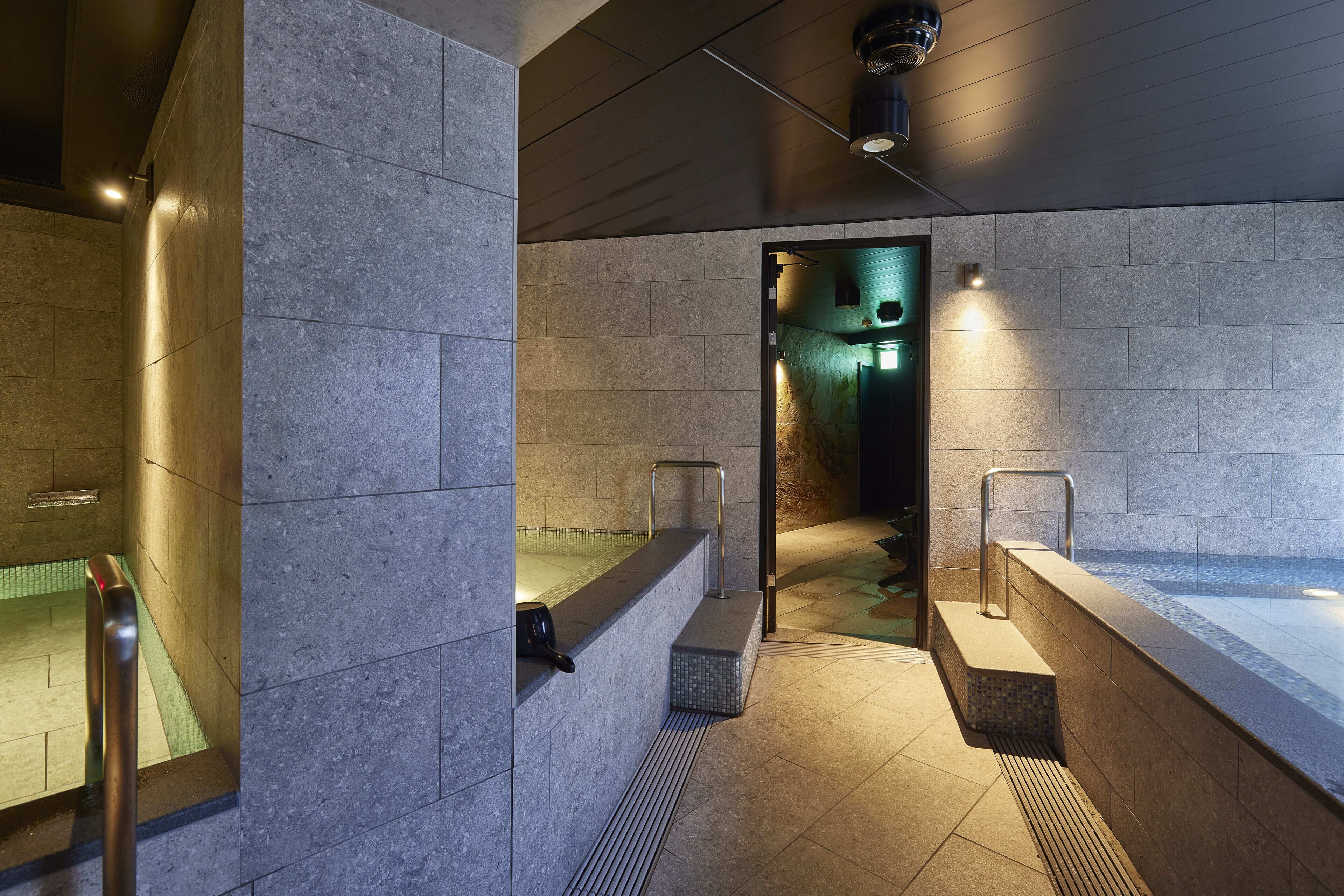 A modern bathroom with stone walls, a heated floor, and a glass-enclosed shower area.