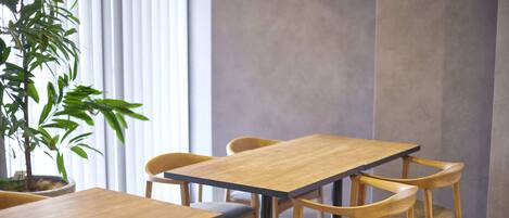 Une salle de conférence avec une table et des chaises en bois, une plante en pot et une fenêtre avec des stores.