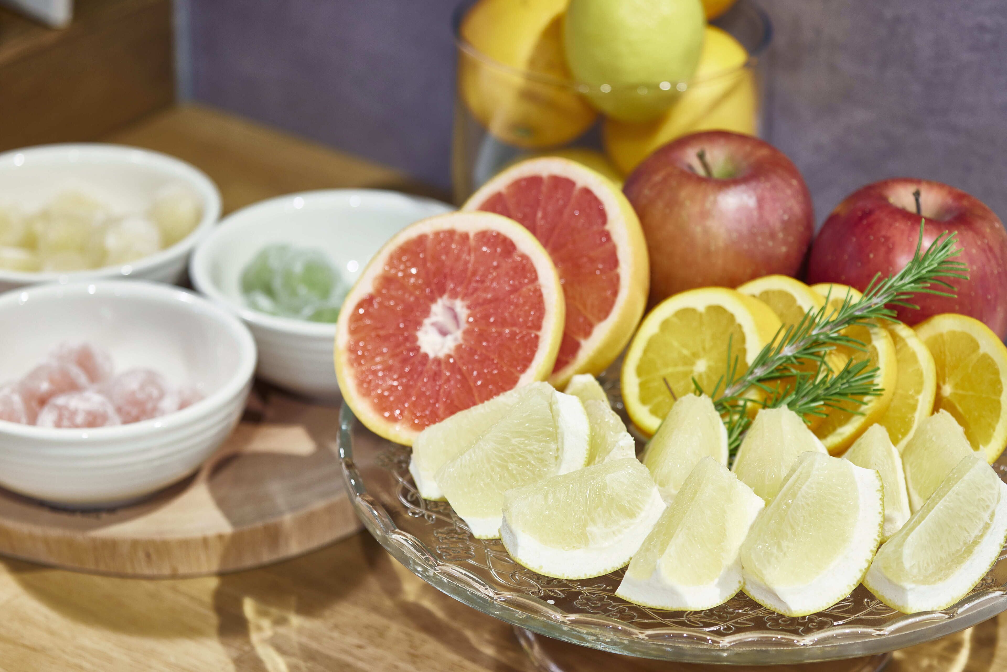 En fruktfat med grapefrukt, äpplen och citronskivor, serverat på en glasskål.