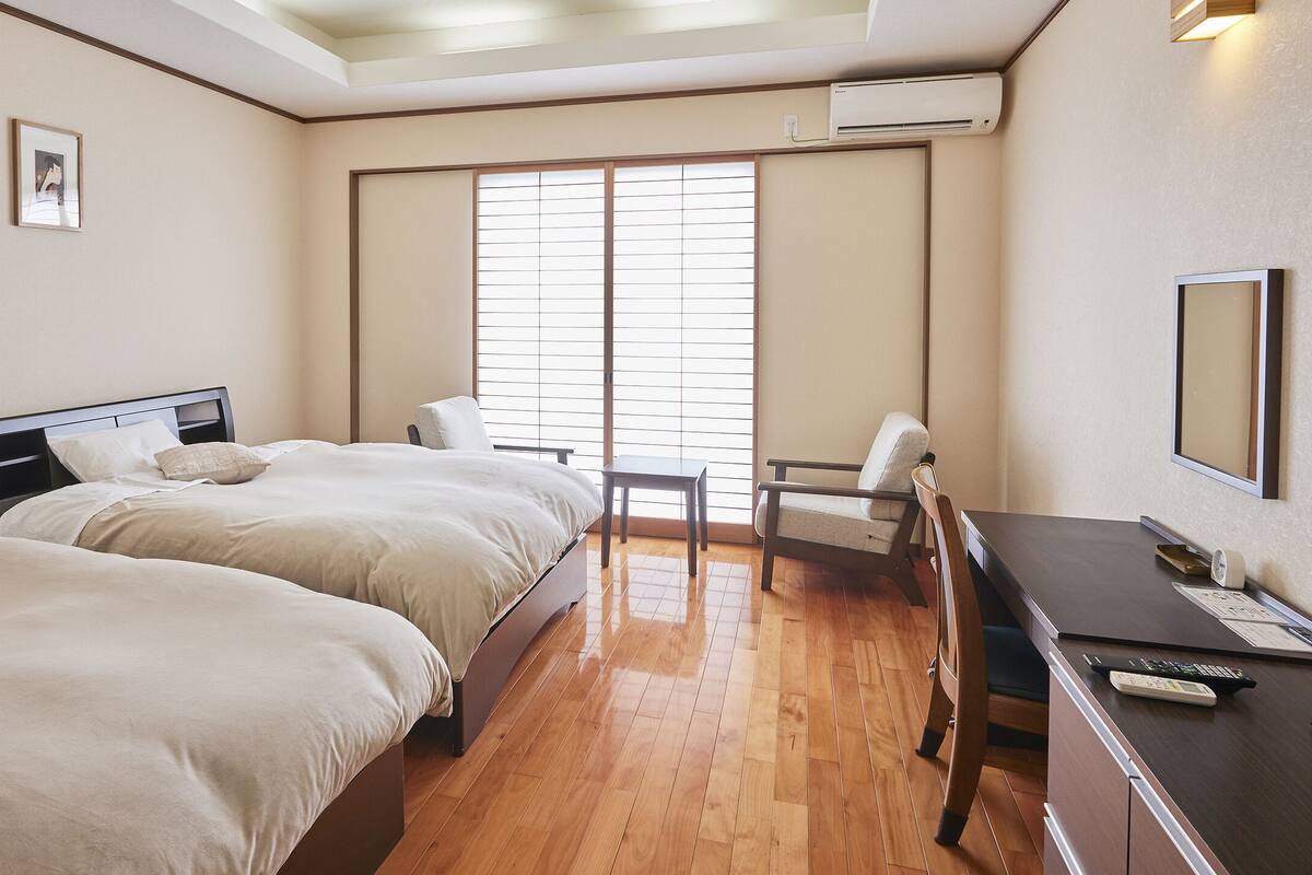Une chambre d’hôtel avec deux lits, un bureau, une chaise et un téléviseur.