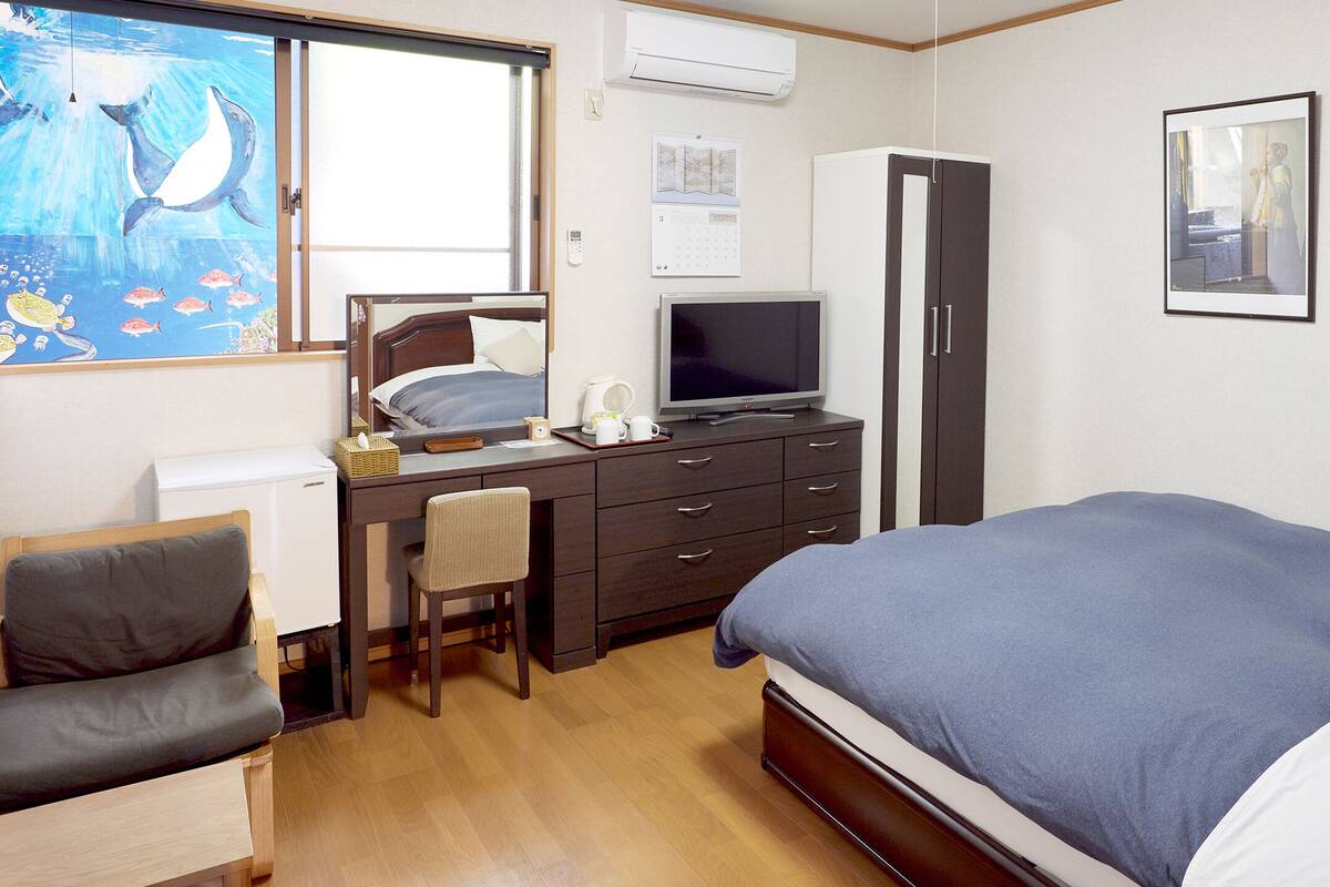 Une chambre d’hôtel comprenant un lit, un bureau avec un ordinateur, une chaise, une télévision et une armoire.