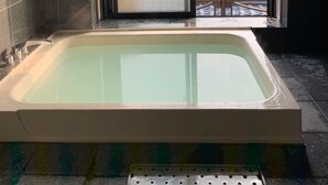 A modern bathroom with a large bathtub, a window with a view of a tiled roof and mountains, and a tiled floor. - Temple Stay Tsushima Seizanji (Tsushima)