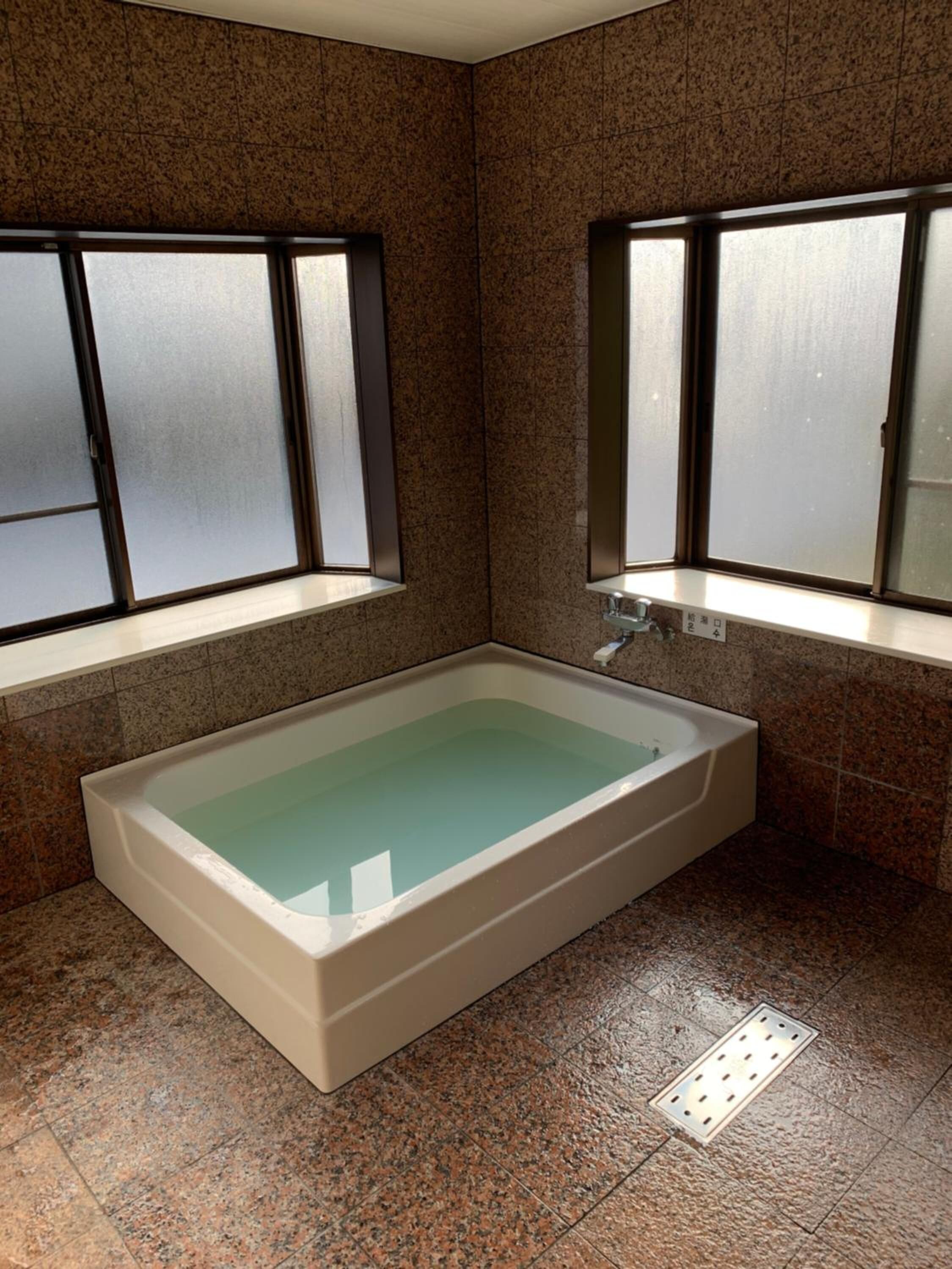 A modern bathroom with a rectangular bathtub, frosted windows, and granite tiles.