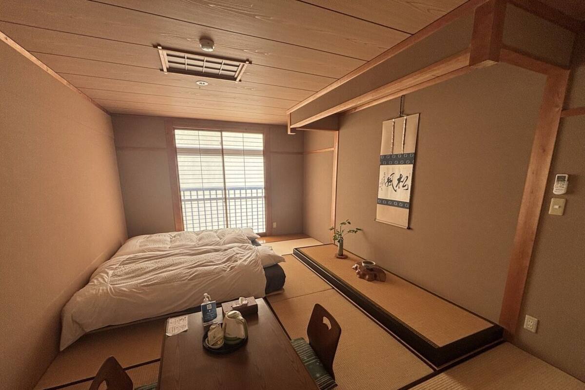 Une pièce de style japonais traditionnel, avec un sol recouvert de tatamis, un futon servant de lit, une petite table en bois et une bouilloire, ainsi qu’un paravent shoji.