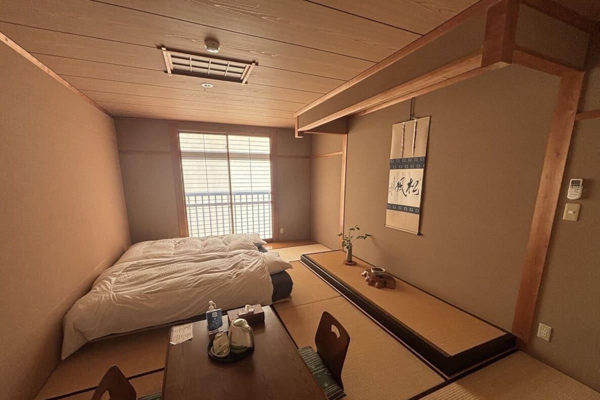 A traditional Japanese room with tatami flooring, a futon bed, a low wooden table with a kettle, and a shoji screen.