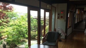A room with wooden flooring, a large window with a view of greenery, a wicker chair, and a table. - Temple Stay Tsushima Seizanji (Tsushima)