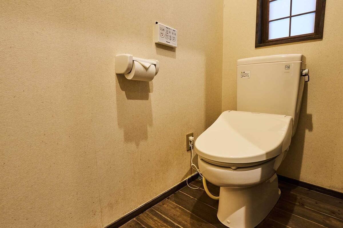 Inodoro con tanque, un rollo de papel higiénico y un enchufe en la pared.
