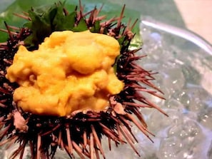 Un oursins de mer, surmonté d’une garniture jaune, présenté sur une assiette en verre.