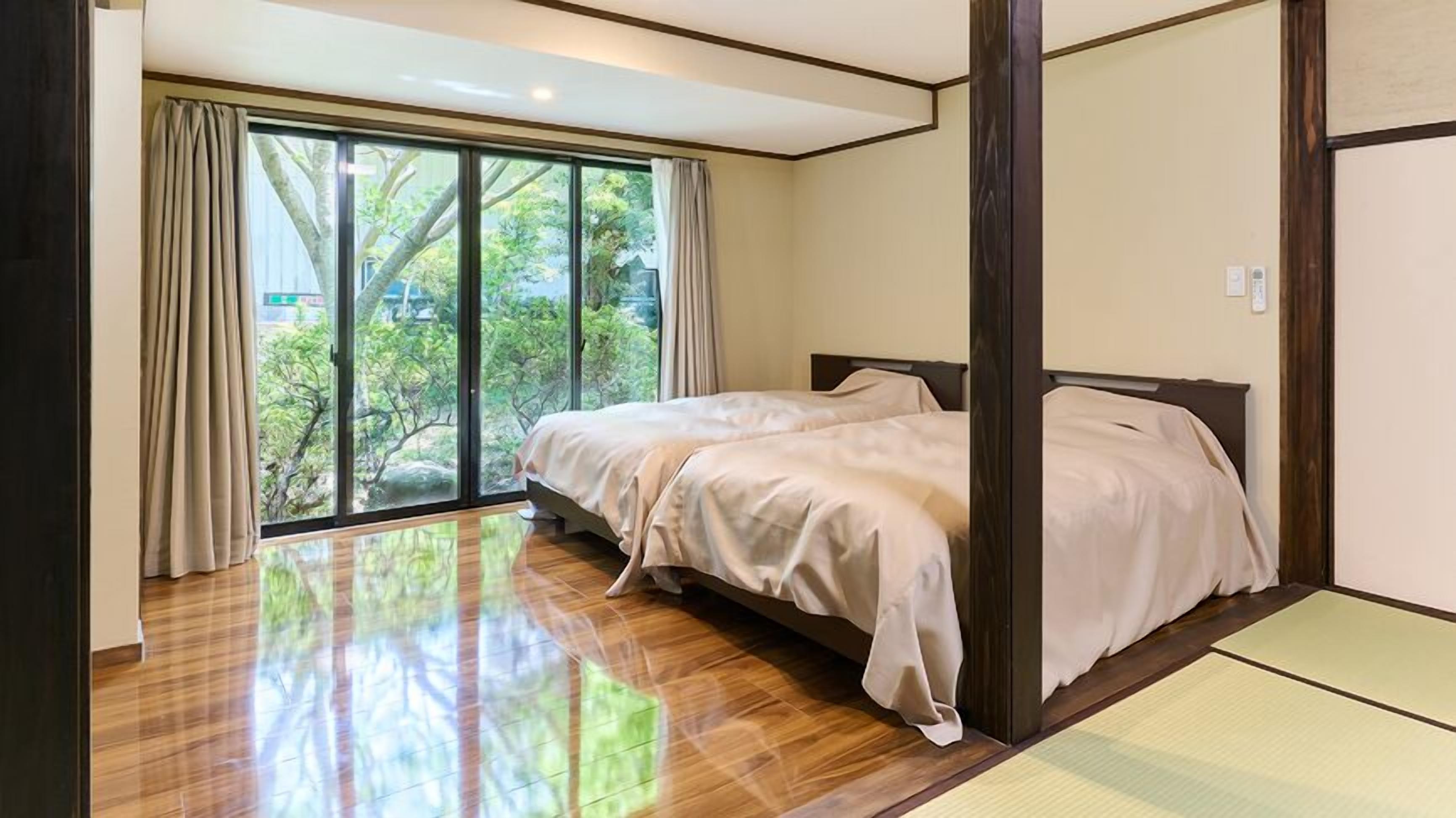 Un dormitorio con un gran ventanal corredera que da a un jardín, una cama con cabecera de madera y un futón en la esquina.