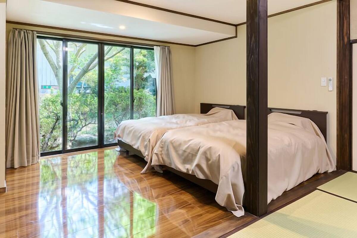 Un dormitorio con un gran ventanal corredera que da a un jardín, una cama con cabecera de madera y un futón en la esquina.