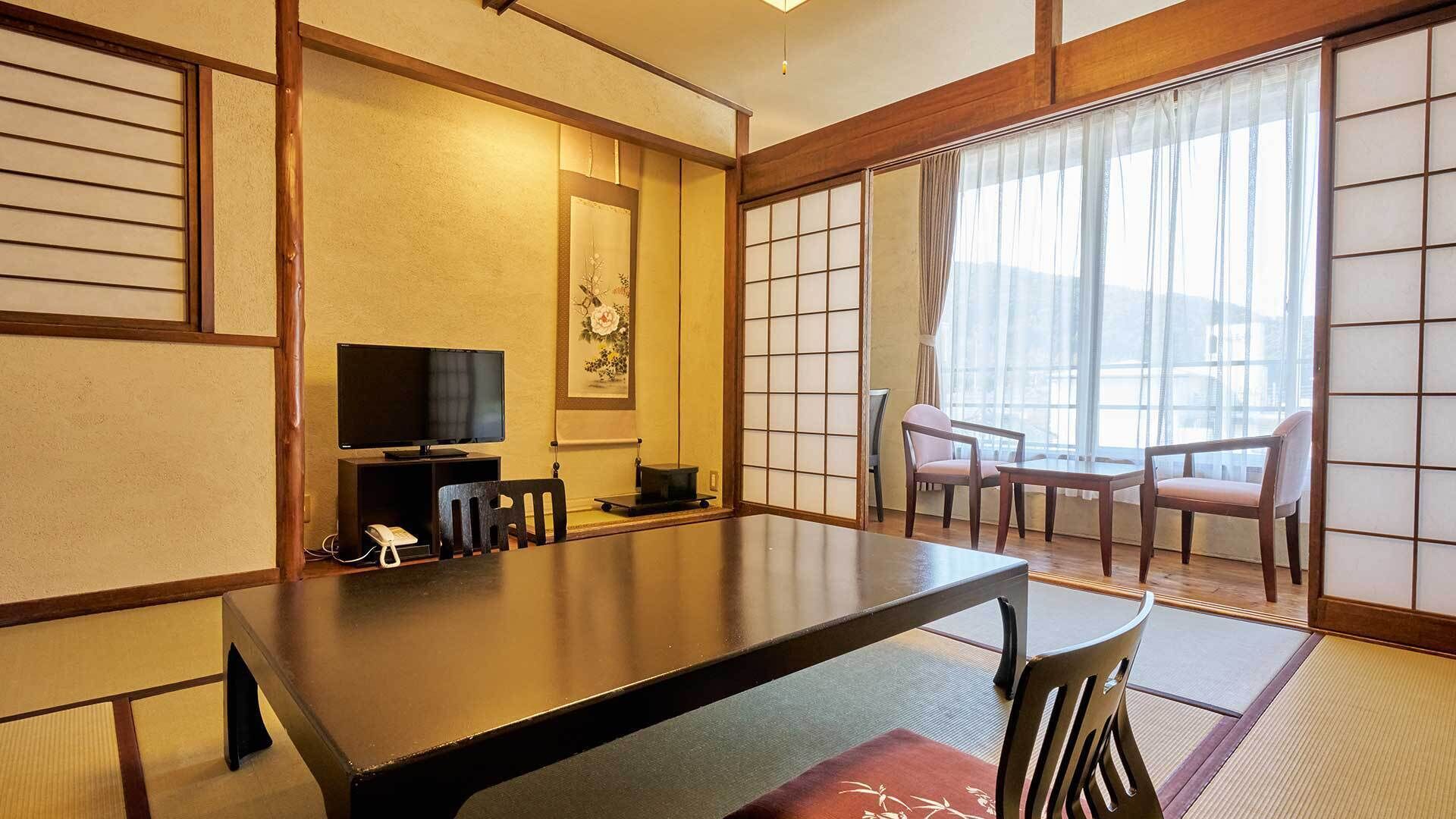 Een traditionele Japanse kamer met tatami vloerbedekking, een lage tafel, een televisie en schuifdeuren.