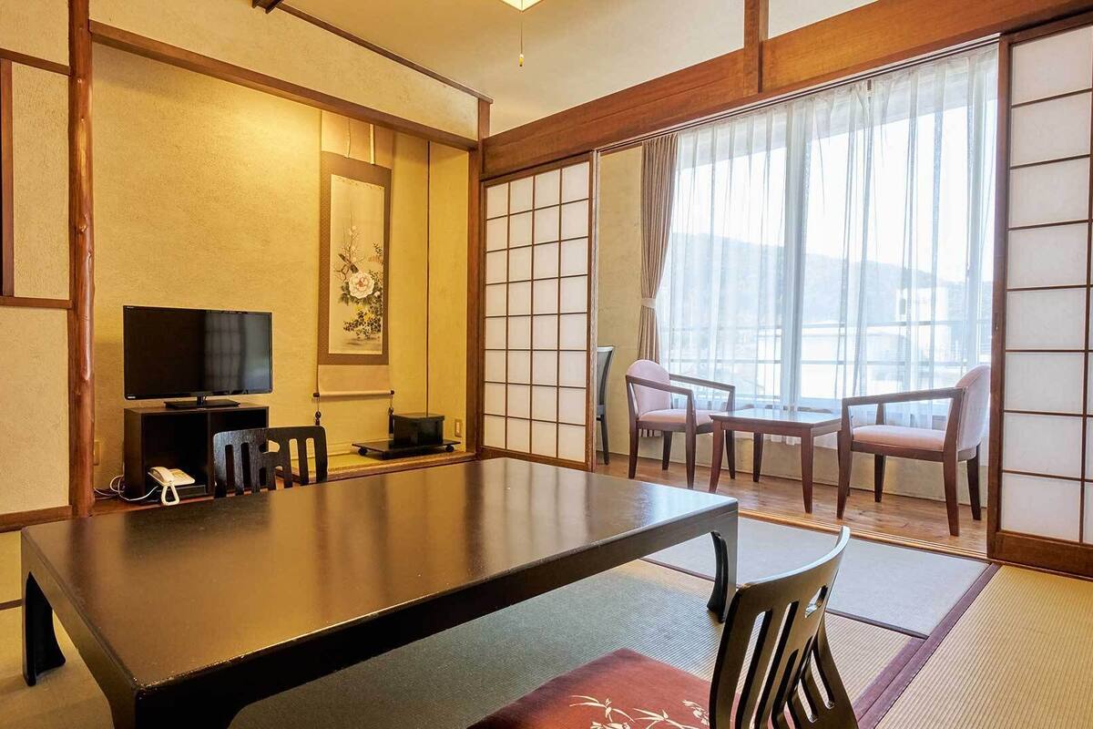Una habitación tradicional japonesa con suelo de tatami, una mesa baja, un televisor y puertas correderas.