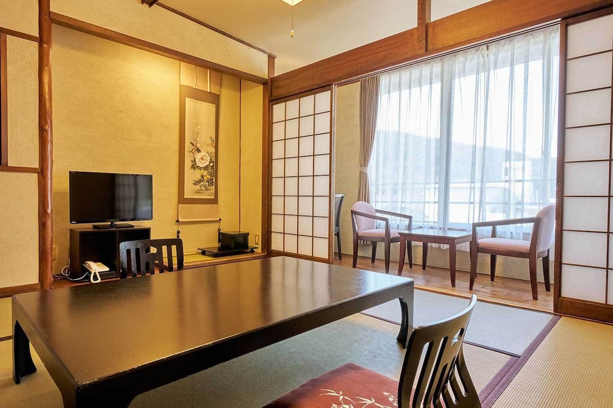 Una habitación tradicional japonesa con suelo de tatami, una mesa baja, un televisor y puertas correderas.