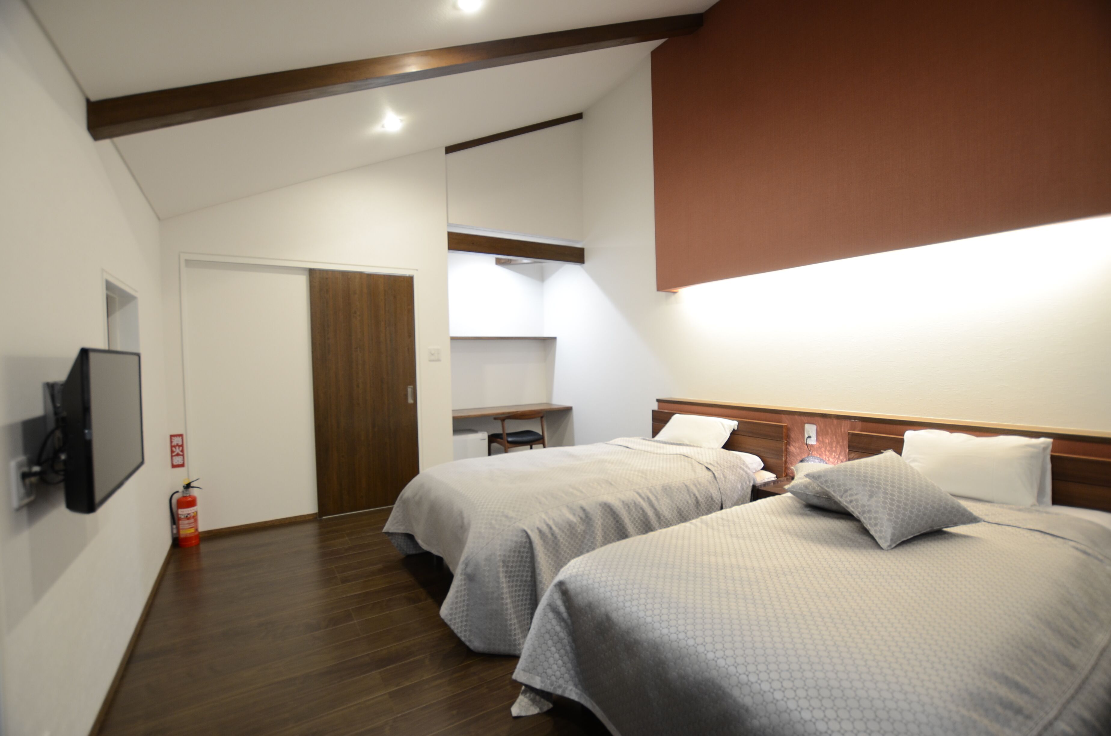 Habitación de hotel con dos camas, un televisor, un extintor y una viga de madera en el techo.