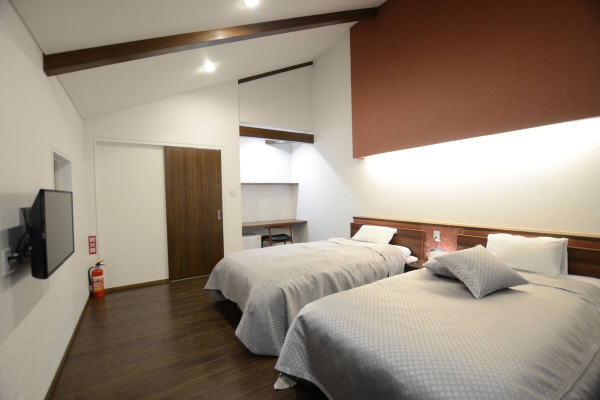 Habitación de hotel con dos camas, un televisor, un extintor y una viga de madera en el techo.